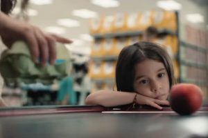 Una bimba guarda una pesca dentro a un supermercato